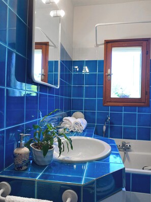 A bathroom with blue tiles, a sink, a mirror, a window, and a bathtub.