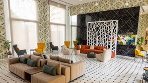 Ein modernes Wohnzimmer mit einem Ecksofa, mehreren Sesseln, einem schwarz-weißen Musterboden und einem großen Fenster mit Vorhängen.