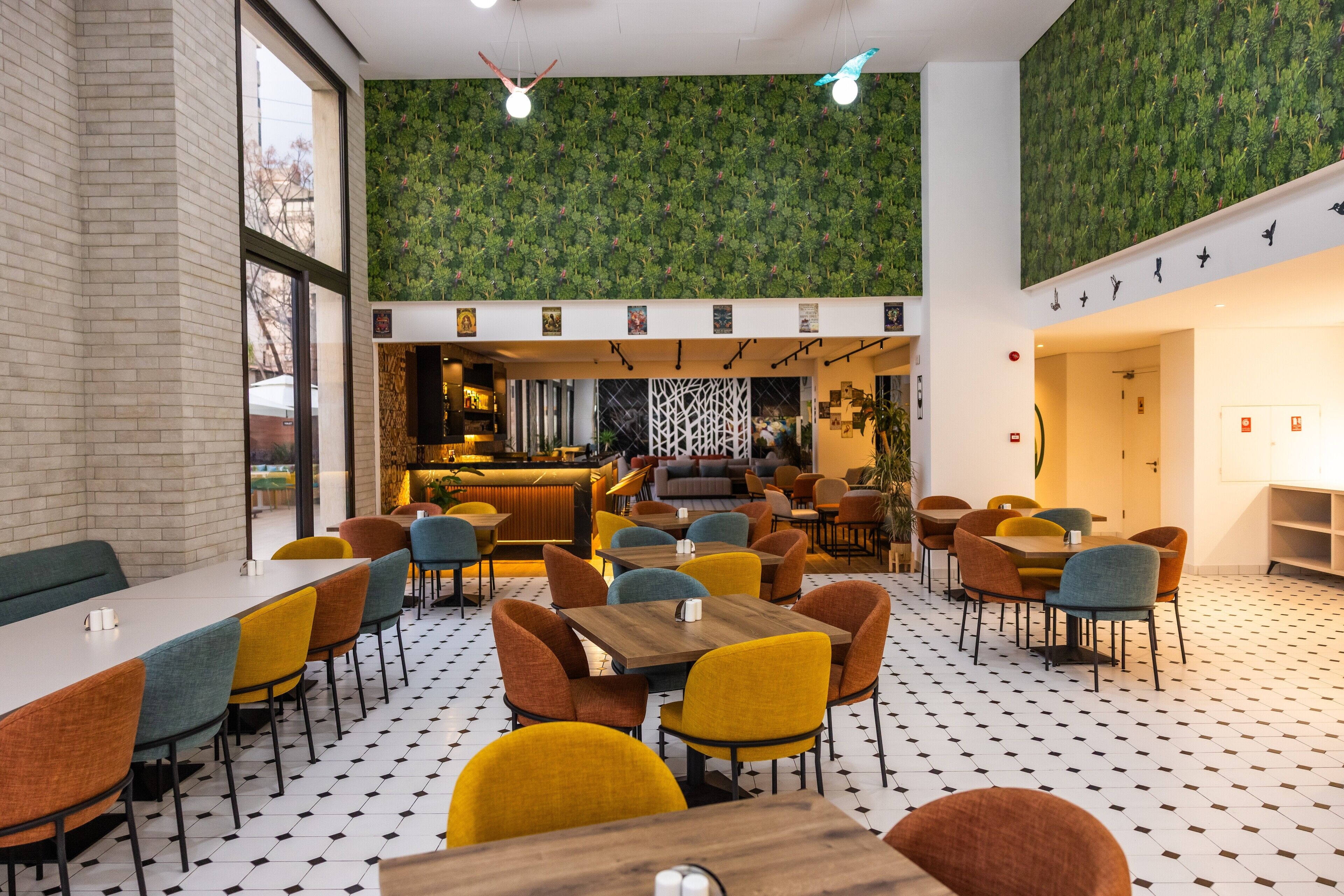 A modern restaurant with a variety of seating options, including tables and booths, and a bar area visible through a glass partition.