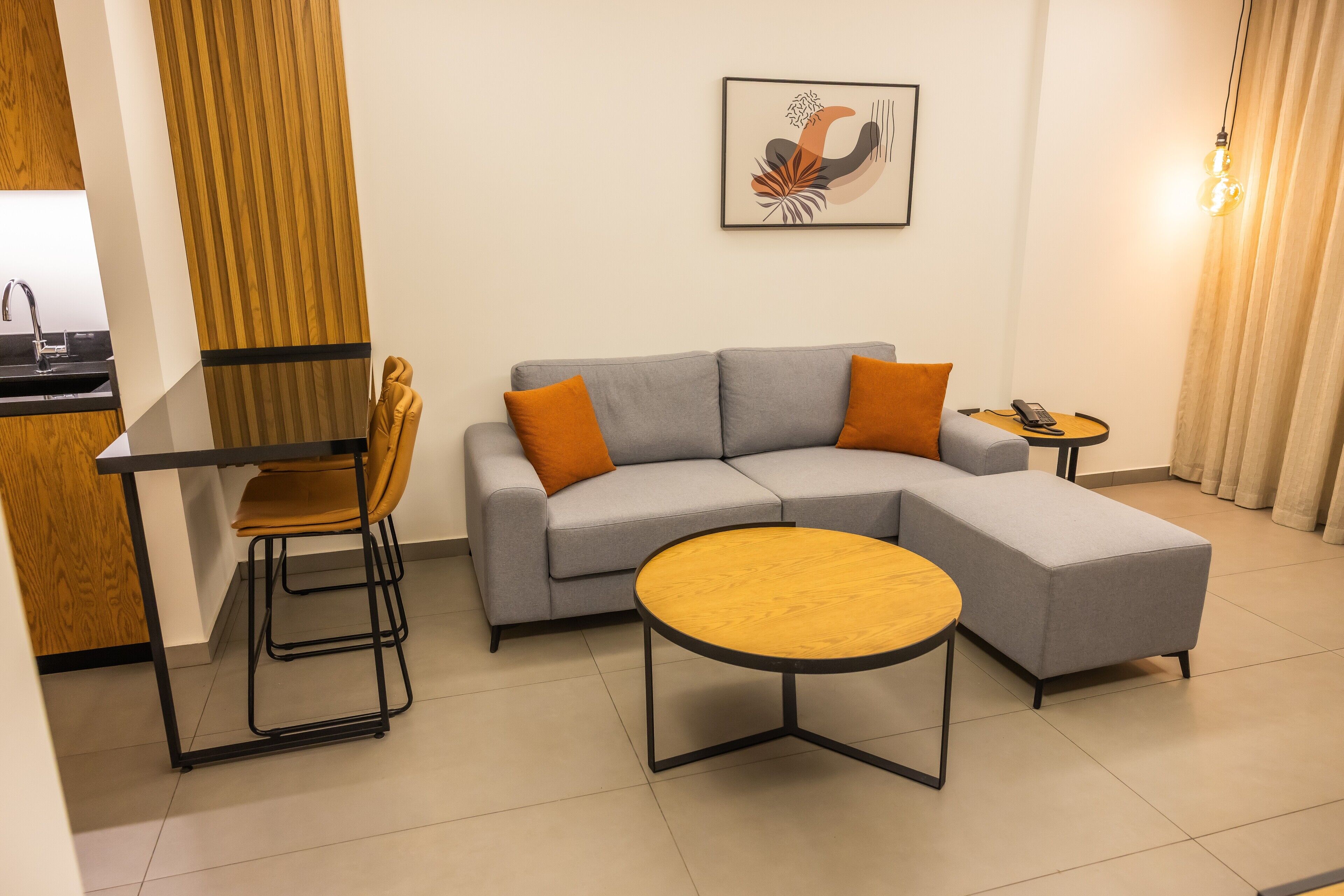 A modern living room with a grey sectional sofa, a wooden coffee table, a small round table, and a bar stool.