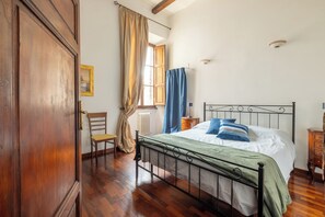A bedroom with a wooden floor, a metal bed frame, a window with curtains, a radiator, and a wooden cabinet. - New luxury apartment for groups and families in the heart of Rome (Roma)