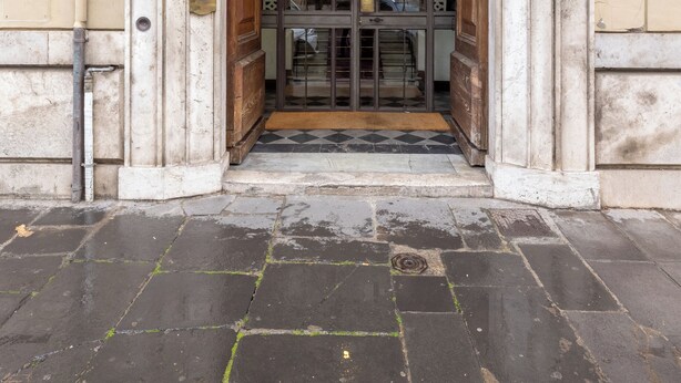 An ornate entrance with a large arched doorway, a tiled floor, and a brick wall.