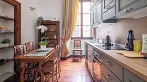 A compact kitchen with wooden cabinets, a dining table with chairs, and a window with curtains.