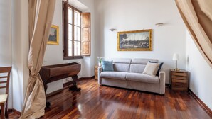 A room with a wooden floor, a sofa, a bench, a table, and a window with curtains.
