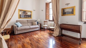 A room with a wooden floor, a sofa, a chair, a wooden bench, and two paintings on the walls.