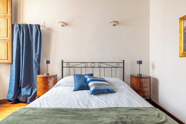 A neatly made bed with a white and blue striped bedspread, two pillows, and a green throw blanket. There are two wooden nightstands with lamps and a metal headboard. - New luxury apartment for groups and families in the heart of Rome (Roma)