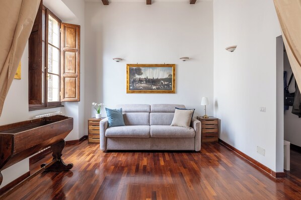 Un salon avec un plancher en bois, un canapé, un banc en bois et un tableau accroché au mur.