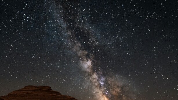 Paisaje desértico con una terraza de madera que conduce a varias cabañas pequeñas con techos oscuros bajo un cielo estrellado.