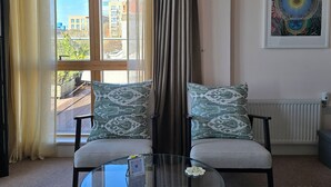 Un salon avec un canapé, une table basse en verre et une vue sur les immeubles à travers de grandes fenêtres.