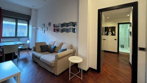 Un salon moderne avec un canapé, une petite table et un coin repas avec des chaises. Un couloir mène à une salle de bain.