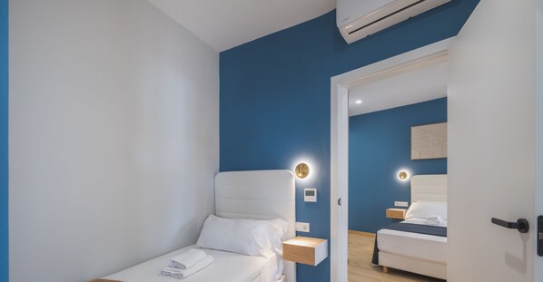 A modern hotel room with a single bed, bedside tables, and a wall-mounted air conditioner.