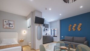 Una habitación de hotel moderna con una cama, una mesa de comedor de vidrio, un sofá, una cocina y una pared decorada en azul.