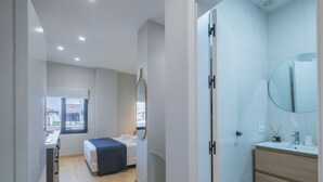 Una habitación de hotel moderna con una cama grande, una mesita de noche, un espejo y un baño con lavabo y espejo.