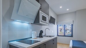 Una cocina moderna con estufa integrada, microondas y hervidor, un lavamanos y un ventanal con vistas a la calle.
