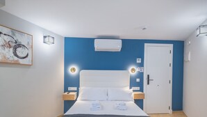 Une chambre d’hôtel moderne avec un grand lit, un mur d’accent bleu, un appareil de climatisation, une table de chevet avec une lampe et un tableau au mur.