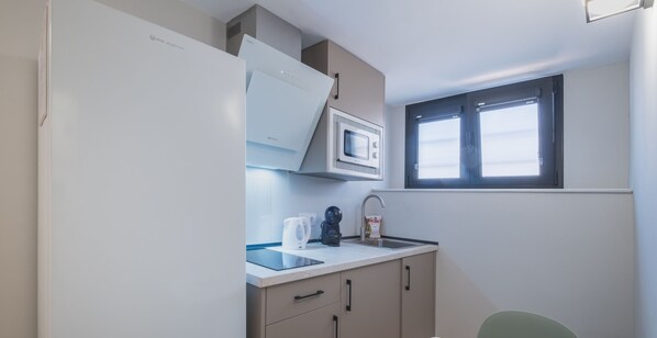 Eine kompakte Küchenzeile mit Mikrowelle, Wasserkocher und Spüle. Ein kleines Fenster.
