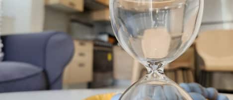 An hourglass surrounded by blue objects on a table in a modern kitchen with cabinets and a dining area in the background.