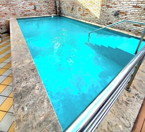 Une piscine rectangulaire avec un bord carrelé et un escalier en métal.