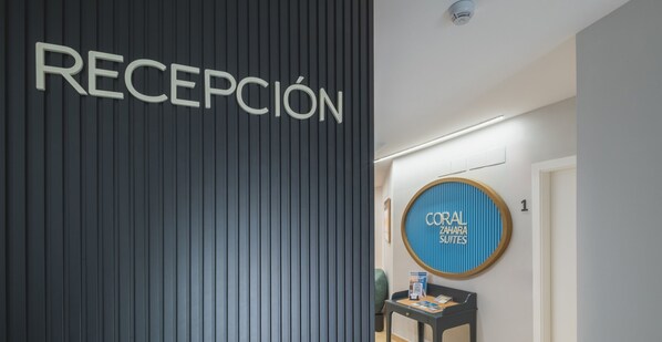 A reception area with a vertical panel labeled "RECEPCIÓN" and a circular sign for "CORAL ZAHARA SUITES". - Estudio Cuadruple - CORAL ZAHARA Suites by Cadiz4Rentals (Zahara de los Atunes)