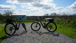 Two bicycles parked on a gravel path with a green building and a field in the background. - Primrose (With Hot-Tub) (Reynalton)