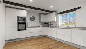 A modern kitchen with white cabinets, a microwave, an oven, and a clock on the wall. - Foxen Holes, Foxenholes cottage, Saundersfoot (Saundersfoot)