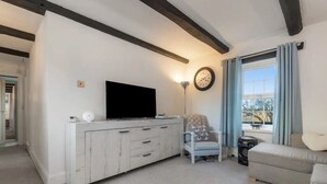 A living room with a white entertainment unit, a flat-screen TV, a clock, a chair, a sofa, and a window with curtains. - Foxen Holes, Foxenholes cottage, Saundersfoot (Saundersfoot)