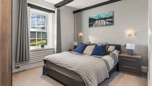 A bedroom with a large bed, bedside tables, a window with curtains, and a painting on the wall. - Foxen Holes, Foxenholes cottage, Saundersfoot (Saundersfoot)