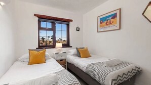 A bedroom with two beds, a window with a view, a lamp, and a framed picture on the wall.