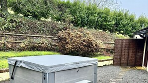 A grey mattress with a built-in step-up feature, placed on a gravel surface with a wooden fence and greenery in the background.