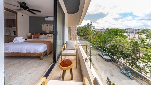 Une chambre d’hôtel moderne dotée d’un grand lit, d’un balcon offrant une vue sur la ville et d’une petite table avec une chaise.