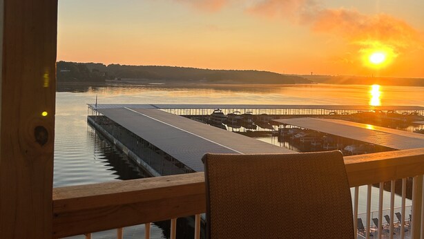 Une vue depuis un balcon donnant sur un coucher de soleil au-dessus d’une étendue d’eau, avec un quai et une jetée.
