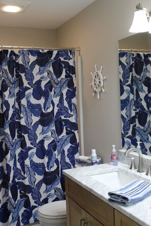 Ein Badezimmer mit Duschvorhang mit blau-weißem Blattmuster, einer Schiffsschwengel-Dekoration, einem Marmorwaschbecken und einem Handtuch auf der Ablagefläche.