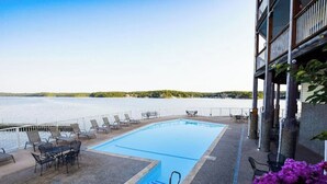 Une piscine dotée de chaises longues et de tables, avec vue sur une étendue d’eau.