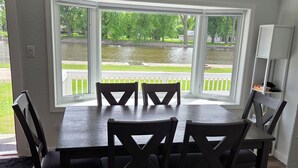 A dining area with a table and chairs, large windows with a view of a pond and greenery, and a white cabinet.