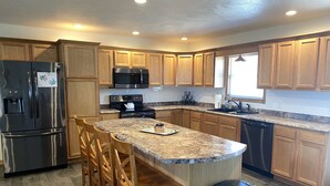 A modern kitchen with wooden cabinets, stainless steel appliances, granite countertops, and a central island with bar stools.