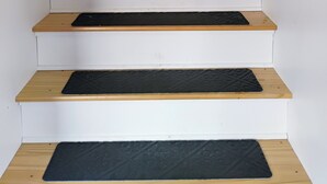 Una escalera con escalones de madera y un felpudo negro al final.