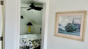 Un dormitorio con cama, ventilador de techo, lámpara y un cuadro en la pared.