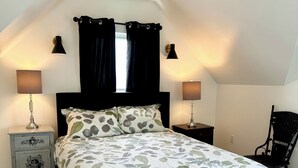 Un dormitorio con cama, dos mesitas de noche, una silla y una ventana con cortinas.