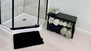 Un baño moderno con cabina de ducha de vidrio, un perchero negro con toallas y un cuadro en la pared.