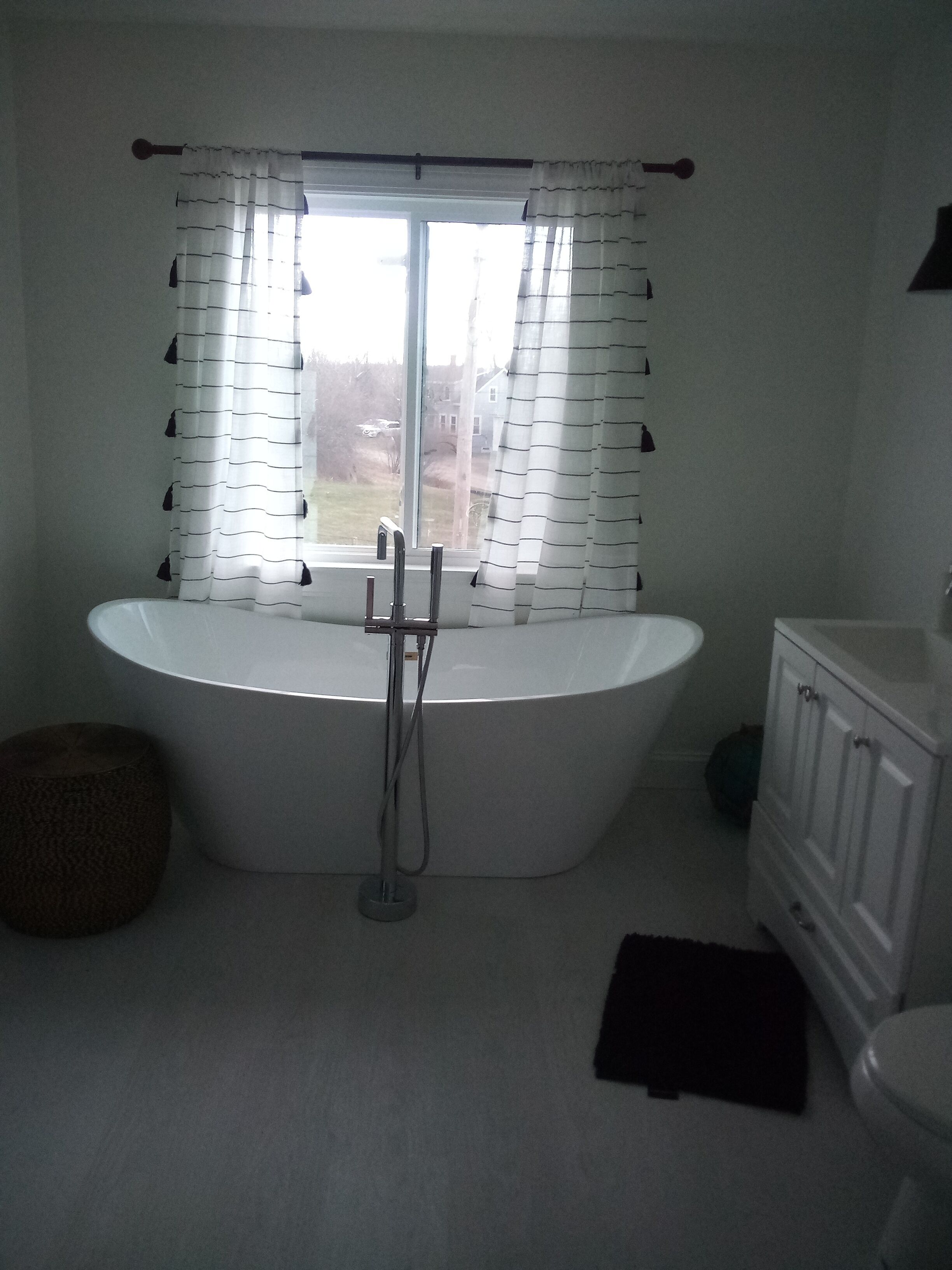 A bathroom with a freestanding bathtub, a window with striped curtains, a white sink, and a cabinet.