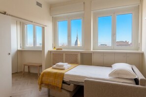 A hotel room with a bed, a small table, and a window with a city view.
