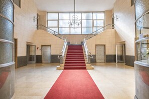 A grand staircase with a red carpet leading to an upper floor, flanked by glass doors and a modern light fixture. - DomusNova Finestra Penthouse historic center Turin (Torino)