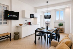 A modern kitchen with a flat-screen TV, a dining area with a table set for four, and a view of a cityscape through large windows.