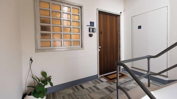 L’entrée d’un hôtel avec une porte en bois, une fenêtre à carreaux, une plante en pot et un sol carrelé.