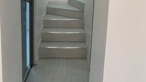 Escada que leva a um andar superior, com uma parede branca lisa e uma porta à esquerda.