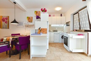 A compact kitchen with white cabinets, a dining area with purple chairs, and a washing machine. - Charming Accommodation With Shared Pool Beahost (Vodnjan)