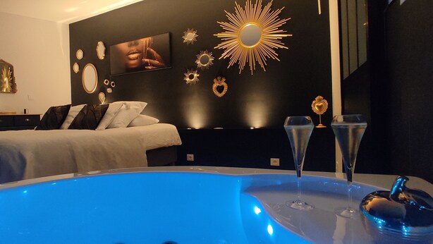 A modern bedroom with a large bed, a wall-mounted TV, decorative mirrors, and a blue-lit hot tub. - Accommodation with a landscaped patio with trees. Ideal for a moment for two. (Ailly-sur-Noye)