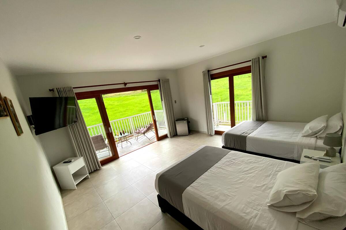 Hotelkamer met twee bedden, een televisie, een kleintje tafel en een balkon met uitzicht op een groen gazon.
