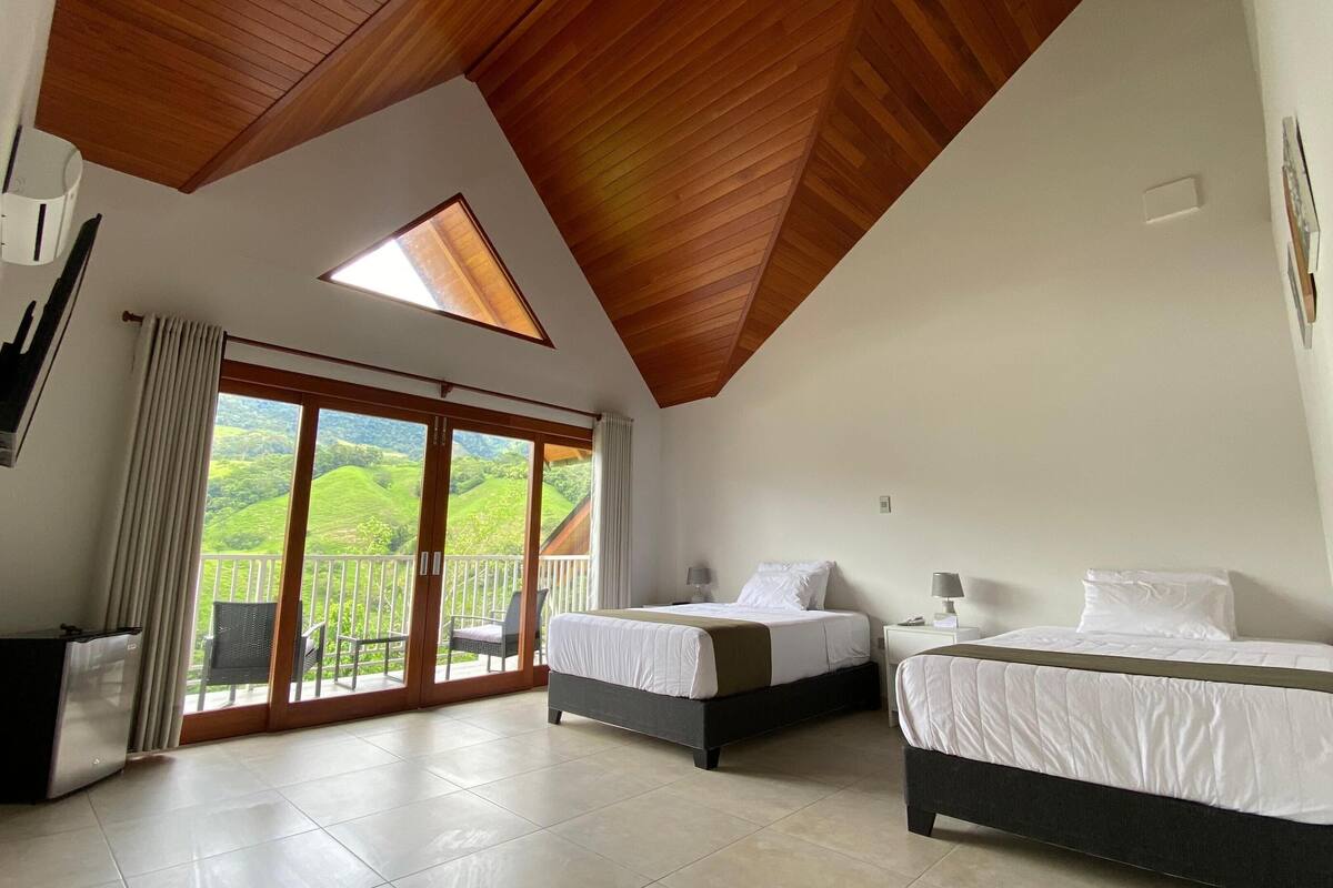 Een slaapkamer met twee bedden, een grote schuifdeur naar een balkon en een plafond met houten balken.