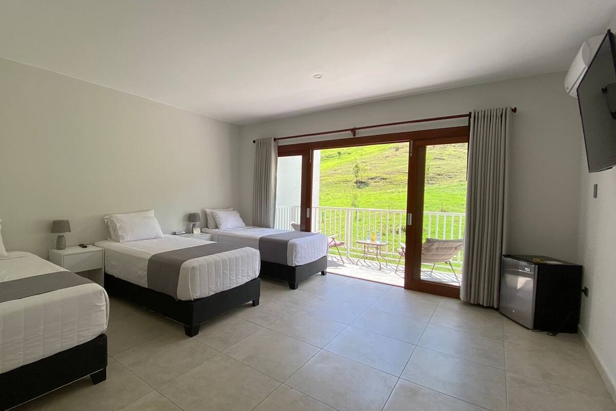 Een hotelkamer met twee bedden, een balkon en uitzicht op een groen landschap, plus een kleine koelkast.